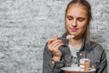 Young teenager brunette girl with long hair eating slice cake dessert on gray wall background Royalty Free Stock Photo