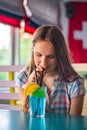 Teenager brunette girl with long hair holding a glass with a blue lemonade cocktail with fruits at a table in cafe Royalty Free Stock Photo