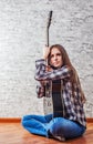 Teenager brunette girl with long hair sitting on the floor and playing an black acoustic guitar on gray wall background Royalty Free Stock Photo