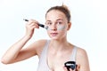 Young teenager girl applying facial mask using brush, on white background.