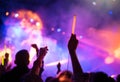 Young teenager girl fan raised up two hands with colored glowing sticks supporting favorite popular band on the night concert. Col