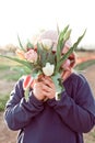 Young teenager girl hiding behind a bunch of tulips. Sunset outdoor scene, family outdoor activity time