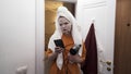 Young teenager girl leaving the bathroom at home with a towel on her head, holding smartphone and hairdryer. Action Royalty Free Stock Photo