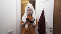 Young teenager girl leaving the bathroom at home with a towel on her head, holding smartphone and hairdryer. Action Royalty Free Stock Photo