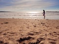 Young teenager girl silhouette running at ocean water. Sandy beach and sky. Royalty Free Stock Photo