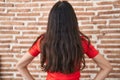 Young teenager girl standing over bricks wall standing backwards looking away with arms on body Royalty Free Stock Photo