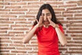 Young teenager girl standing over bricks wall shouting angry out loud with hands over mouth Royalty Free Stock Photo