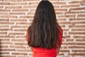 Young teenager girl standing over bricks wall standing backwards looking away with crossed arms Royalty Free Stock Photo