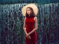Young teenager girl in stylish red dress in unique location in water and water fall in the background. Lady in high fashion outfit
