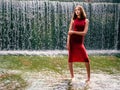 Young teenager girl in stylish red dress in unique location in water and water fall in the background. Lady in high fashion outfit