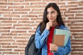 Young teenager girl wearing student backpack and holding books serious face thinking about question with hand on chin, thoughtful Royalty Free Stock Photo