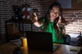 Young teenager girl working at the office at night looking at the camera smiling with open arms for hug Royalty Free Stock Photo