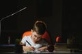 Young teenager schoolboy at the table doing homework in the dark room Royalty Free Stock Photo