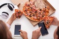 Young teenagers checking their phones while eating pizza