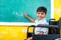 Young teenger school kid with disability on wheel chair writing on board while looking at camera - concept of education