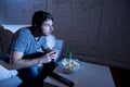 Young television addict man sitting on home sofa watching TV eating popcorn and drinking beer bottle