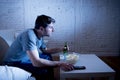 Young television addict man sitting on home sofa watching TV eating popcorn and drinking beer bottle