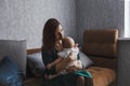 A young gentle happy mother hugs her newborn baby, smiling, sitting at home on the couch. Royalty Free Stock Photo