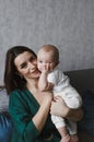 A young gentle happy mother hugs her newborn baby, smiling, sitting at home on the couch. Royalty Free Stock Photo