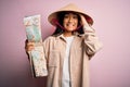 Young thai tourist woman on vacation wearing traditional conical asian hat holding city map stressed with hand on head, shocked Royalty Free Stock Photo