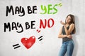 Young thinking brunette girl wearing casual jeans and t-shirt with `Maybe yes maybe no` sign and cartoon heart on white