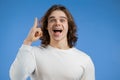 Young thinking pondering man having idea moment pointing finger up on blue studio background. Smiling happy guy showing Royalty Free Stock Photo
