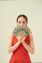 Young thinking pretty woman in red dress hiding behind bunch of money banknotes,  on bright background Royalty Free Stock Photo