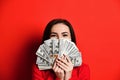Young thinking pretty woman in red dress hiding behind bunch of money banknotes Royalty Free Stock Photo