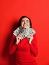 Young thinking pretty woman in red dress presses to herself a bunch of money banknotes Royalty Free Stock Photo