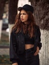 Young thinking teen hipster woman looking near the tree  on the street background in black style clothing and cool cap. Autumn Royalty Free Stock Photo