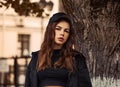 Young thinking teen woman looking near the tree  on the street background in black style clothing and cool cap. Autumn season Royalty Free Stock Photo