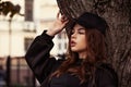 Young thinking teen woman looking near the tree  on the street background in black style clothing and cool cap. Autumn season Royalty Free Stock Photo