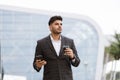 Young thoughtful Arab man standing outside modern building and drinking take away coffee Royalty Free Stock Photo