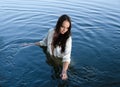 Young thoughtful brunette woman in white shirt is standing in the lake and moving hands through water. Royalty Free Stock Photo