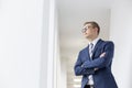 Young thoughtful businessman standing with arms crossed looking away in office corridor Royalty Free Stock Photo