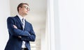 Young thoughtful businessman standing with arms crossed looking away in office corridor Royalty Free Stock Photo