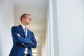 Young thoughtful businessman standing with arms crossed looking away in office corridor Royalty Free Stock Photo