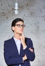 Young thoughtful businesswoman looking at energy efficient lightbulb hanging against brick wall at office Royalty Free Stock Photo