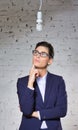 Young thoughtful businesswoman looking at energy efficient lightbulb hanging against brick wall at office Royalty Free Stock Photo