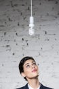 Young thoughtful businesswoman looking at energy efficient lightbulb hanging against brick wall at office