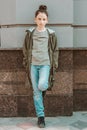 Young thoughtful caucasian girl leaning on an industrial wall. Full-lenght portrait of a pretty model in casual clothes. Street Royalty Free Stock Photo