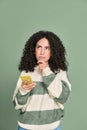Young thoughtful latin woman holding mobile phone thinking  on green. Royalty Free Stock Photo