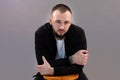 Young thoughtful pensive bearded man with dark hair wearing black jacket, white T-shirt sitting at stool, folding hands. Royalty Free Stock Photo