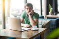 Young thoughtful quizzical businessman in green t-shirt sitting with laptop, hand on chin looking away and thinking what to do Royalty Free Stock Photo