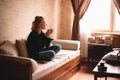 Young thoughtful woman drinking tea and eating chocolate while looking through window sitting at home Royalty Free Stock Photo