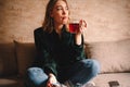 Young thoughtful woman drinking tea and eating chocolate while sitting on sofa Royalty Free Stock Photo