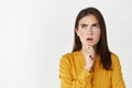 Young thoughtful woman looking up puzzled, touching chin while thinking, searching solution, standing over white Royalty Free Stock Photo