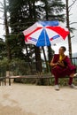 A young Tibetan Buddhist monk sits under an umbrella in Mcleod Ganj, India