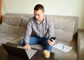 Young tired business man in shirt and trousers sitting on the couch and working with pensive serious face behind laptop after work Royalty Free Stock Photo