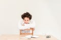 Young, tired Caucasian freelancer man sitting in his home office at the table in front of empty clear wall. Royalty Free Stock Photo